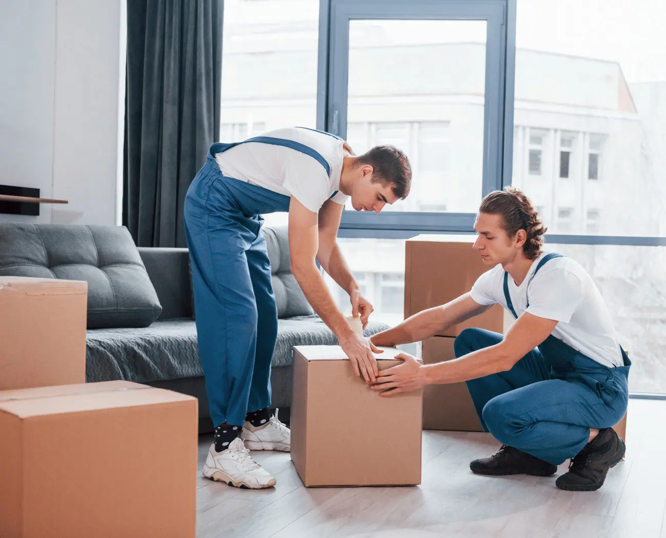Movers sealing boxes in a living room.